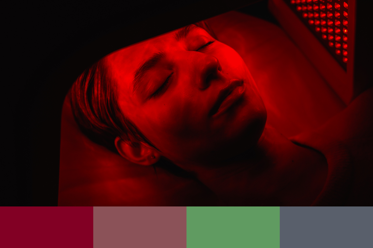 A woman lies on a red light therapy bed. Red light shines on her face gently.